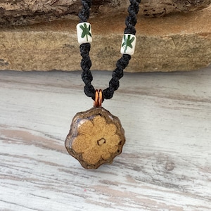 May include: A brown and tan ceramic flower pendant necklace with a black cord and green shamrock beads.