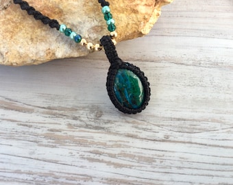 May include: A dark green gemstone pendant necklace with a black cord and gold beads. The pendant is a teardrop shape and is set in a black macrame knot.