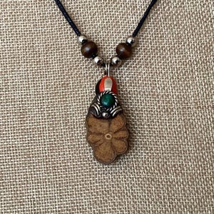 May include: A wooden flower pendant necklace with a green and red stone accent. The necklace is on a black cord with wooden beads.