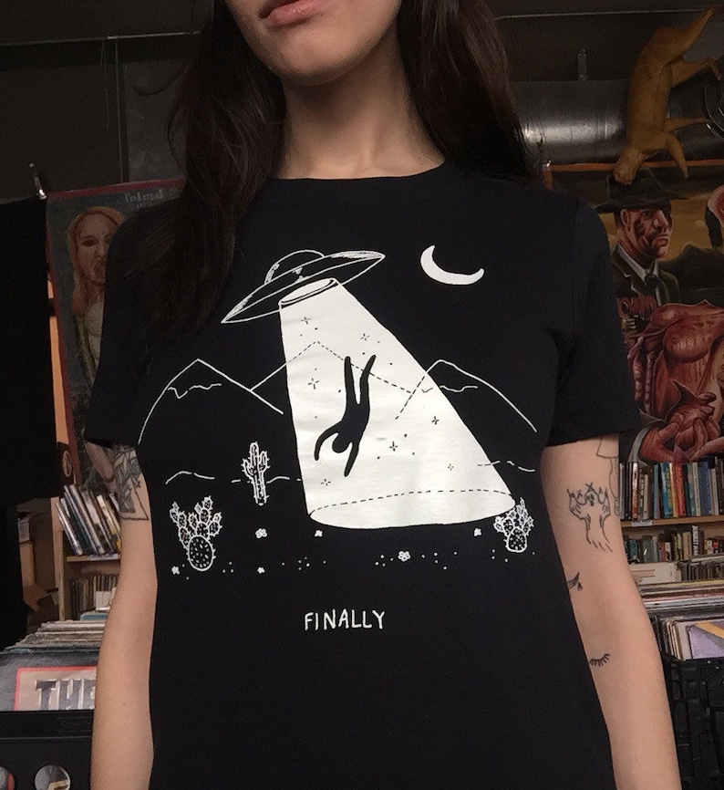May include: Black t-shirt with a white graphic of a person falling from a UFO with the text "FINALLY" underneath.