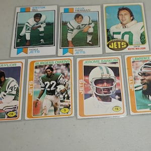 May include: A collection of vintage New York Jets football trading cards. The cards feature images of players in their uniforms, with names and positions printed on the cards. The cards are in various conditions.