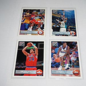 Peut inclure: Quatre cartes de collection de basket-ball représentant des joueurs de la NBA. Les cartes sont blanches avec une bordure bleue et présentent une photo de chaque joueur dans son uniforme. Les cartes comprennent le nom du joueur, son équipe et son poste. Les cartes sont issues de la collection Skybox Premium Basketball 1995-96.