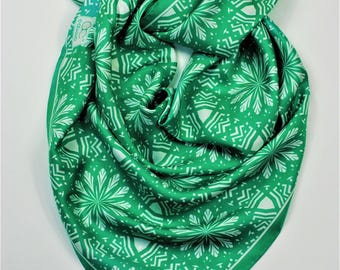 May include: A green and white patterned scarf. The scarf is a square shape, folded and knotted. The pattern is a repeating design of white floral shapes on a green background. The scarf is made of a silky material.