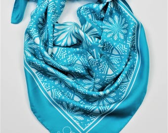 May include: A turquoise blue silk scarf with a white geometric pattern. The scarf has a white label with the text "@alesiac TM" in the lower right corner.