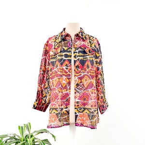 May include: A long-sleeved, sheer button-up shirt with a colorful geometric pattern in shades of pink, orange, yellow, and black. The shirt has a collared neckline and two flap pockets.