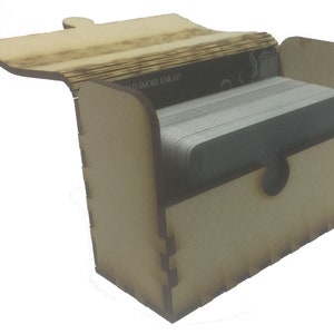 May include: A wooden box with a hinged lid, open to reveal a stack of cards. The box is made of light brown wood and has a simple design. The text "OLD SMOKE KNIGHT" is visible on the box.