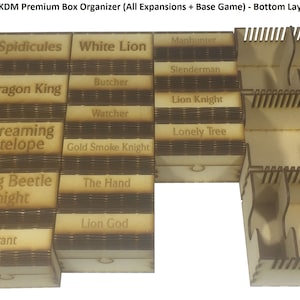 May include: A wooden box organiser for the board game Kingdom Death: Monster. The organiser has compartments labelled with the names of different monsters, including Flower Knight, Spidicules, White Lion, Gorm, Dragon King, Butcher, Watcher, Phoenix, Screaming Antelope, Gold Smoke Knight, Sunstalker, Dung Beetle Knight, The Hand, Lion God, King's Man, and Tyrant.