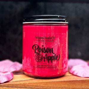 May include: A vibrant red candle in a glass jar with a black lid. The label features the text "Poison Apple" and an apple-skull graphic. The text "Wishes Candle Co" and "a little magic in every candle" are also visible.