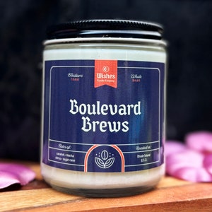 May include: A glass jar candle with a black lid and a navy blue label. The label reads "Boulevard Brews" and includes the text "Medium roast", "Whole bean", and "Notes of: caramel, mocha, citrus, sugar cane". The candle is from Wishes Candle Company.