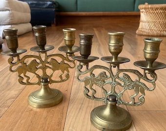 Può includere: Un paio di candelabri antichi in ottone con un design a leone. Ogni candelabro ha quattro bracci per candele e una base rotonda.