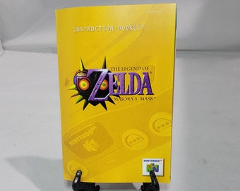 May include: Yellow instruction booklet for the Nintendo 64 video game The Legend of Zelda: Majora's Mask. The cover features a cartoon image of the game's main antagonist, Skull Kid, wearing a mask. The Nintendo 64 logo is in the bottom left corner.