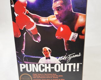 Könnte beinhalten: Eine schwarz-weiße Box für das Nintendo Entertainment System Videospiel "Mike Tyson's Punch-Out!!". Die Box zeigt ein Foto von Mike Tyson in einem Boxkampf. Der Text auf der Box lautet "Mike Tyson's Punch-Out!!" und "Nintendo Entertainment System".