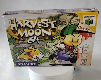 Könnte beinhalten: Eine Harvest Moon 64 Videospielkassette für die Nintendo 64 Konsole. Die Schachtel zeigt einen Comic-Charakter, der mit einem Hund rennt. Der Text auf der Schachtel lautet "Harvest Moon 64" und "Natsume".