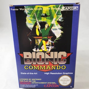 May include: A blue and white Nintendo game cartridge box for the game Bionic Commando. The box features a character holding a gun and a helicopter in the background. The text on the box reads "Bionic Commando", "State-of-the-Art", "High Resolution Graphics", "Licensed by Nintendo for play on the Nintendo Entertainment System", "Game Pak by Capcom", and "Original Nintendo Seal of Quality".
