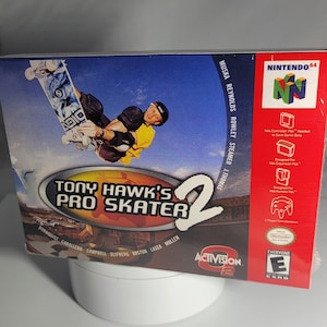 May include: A red, white, and black Nintendo 64 game case for Tony Hawk's Pro Skater 2. The front of the case features a skateboarder performing a trick. The back of the case lists the game's features and credits. The game is rated E for Everyone by the ESRB.