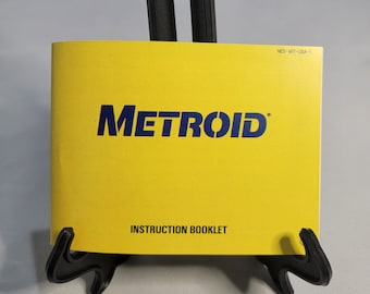 May include: Yellow instruction booklet for the NES game Metroid. The booklet has the title "METROID" in blue letters and the text "INSTRUCTION BOOKLET" in black letters.