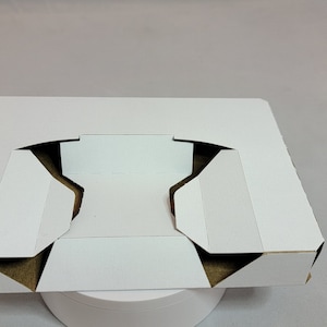 May include: White cardboard box with a cutout in the center, folded into a tray shape.