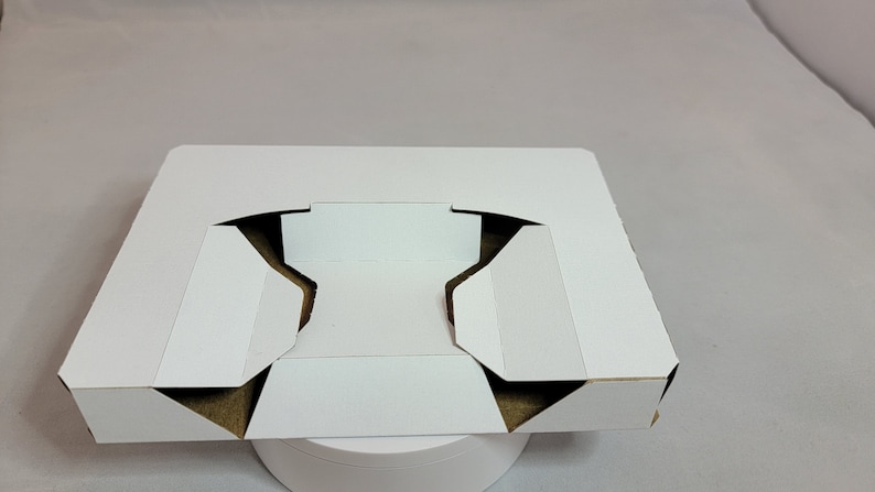 May include: White cardboard box with a cutout in the center, folded into a tray shape.