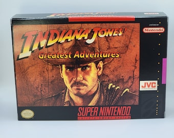 May include: A black and white box for the Super Nintendo Entertainment System video game Indiana Jones' Greatest Adventures. The box features a portrait of Indiana Jones in a brown fedora and a brown leather jacket. The game is licensed by Nintendo and published by JVC.