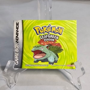 May include: A green and yellow Game Boy Advance instruction booklet for the Pokemon Leaf Green Version game. The cover features a cartoon image of a green Pokemon with a red flower on its head.