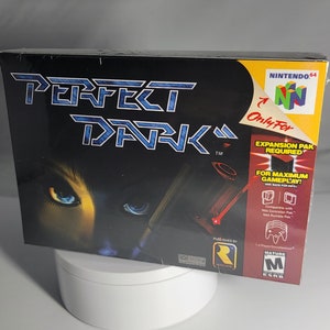 Peut inclure: Une cartouche de jeu Nintendo 64 pour Perfect Dark, un pack d'extension est requis pour jouer. Le jeu est classé M pour Mature. La jaquette présente une femme aux yeux bleus sur un fond sombre.