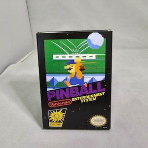 May include: A black Nintendo Entertainment System game cartridge box with a yellow starburst logo and the text "Action Series". The front of the box features a pixelated image of a character playing pinball. The game title is "Pinball" and the text "Nintendo Entertainment System" is printed below the title.