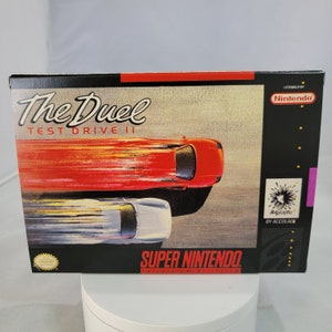 May include: Super Nintendo Entertainment System game cartridge box art for The Duel: Test Drive II. The box features a red and white sports car racing against a silver sports car on a black and white racetrack. The game is licensed by Nintendo and developed by Acclaim.