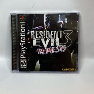 Könnte beinhalten: PlayStation-Spielhülle für Resident Evil 3: Nemesis. Das Cover zeigt eine bedrohliche Kreatur und den Titel des Spiels in einer kräftigen, stilisierten Schriftart. Die Hülle befindet sich in einer transparenten Kunststoffhülle.