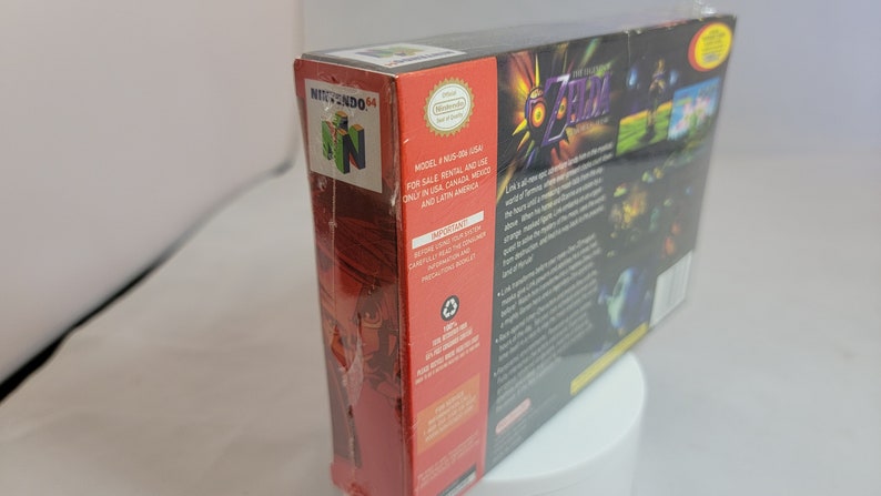 Pu&ograve; includere: Scatola sigillata del videogioco per Nintendo 64 di The Legend of Zelda: Majora's Mask. La scatola &egrave; rossa e nera con dettagli del gioco e un logo Nintendo 64. Il titolo del gioco &egrave; in un font stilizzato con una combinazione di colori oro e viola.
