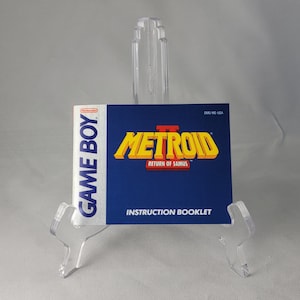 May include: A blue Game Boy instruction booklet for Metroid II: Return of Samus. The booklet has a yellow and red title with the text "Metroid II: Return of Samus" and the text "Instruction Booklet".