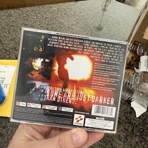 May include: A video game case with the title "Silent Hill" is held in a hand. The cover art features a silhouetted figure and the text "Every town has its secrets, some are just darker than others."