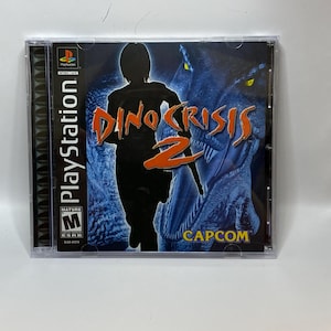 May include: Dino Crisis 2 PlayStation game case. The cover features a silhouetted figure running with the game title in orange and a dinosaur graphic in the background. The case is in a clear plastic jewel case.