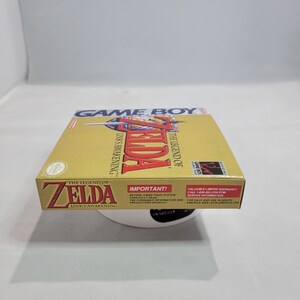 May include: A gold Game Boy cartridge case for The Legend of Zelda: Link's Awakening. The case has a picture of Link on the front with the game title and logo. The back of the case has important information about the game and warranty.