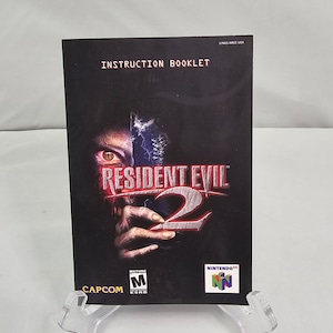 May include: Instruction booklet for the video game Resident Evil 2 for the Nintendo 64. The cover features a zombie face with a red eye and the game title in red and white. The ESRB rating of Mature is visible in the bottom left corner.