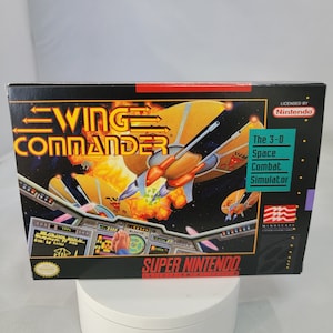 以下が含まれることがあります： スーパーファミコン用ゲームカートリッジ「ウイングコマンダー」。3D宇宙戦闘シミュレーター。パッケージには、オレンジ色の爆発と共に宇宙戦闘中の宇宙船が描かれている。