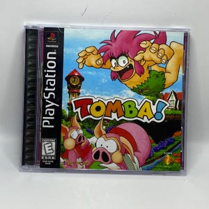 Peut inclure: Boîtier de jeu PlayStation pour Tomba ! avec un personnage de dessin animé aux cheveux roses et un pagne vert. La couverture comprend le titre du jeu et des images de cochons de dessins animés. Le boîtier est dans un étui en plastique transparent.