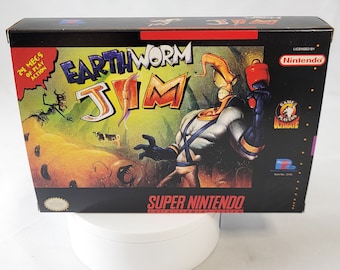 May include: A black Super Nintendo game cartridge box with a colorful image of a cartoon worm character wearing a blue and white suit and holding a red weapon. The box has the title "Earthworm Jim" and the text "24 megs of play action".