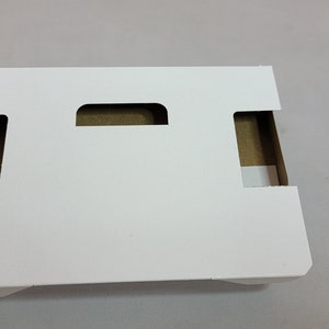 May include: White cardboard box with two cut-out handles. The box is designed to hold and protect items during shipping.