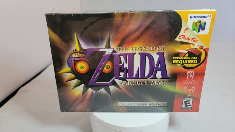 Pu&ograve; includere: Scatola del videogioco The Legend of Zelda: Majora's Mask Collector's Edition. La scatola presenta una maschera con occhi arancioni e il titolo del gioco in viola. Il logo Nintendo 64 &egrave; visibile.