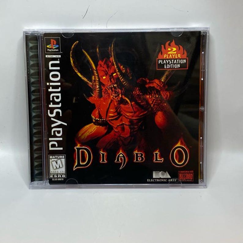 Peut inclure: Bo&icirc;tier de jeu PlayStation pour Diablo. La couverture pr&eacute;sente un d&eacute;mon rouge avec des cornes et le titre du jeu dans une police stylis&eacute;e. Le bo&icirc;tier est &eacute;tiquet&eacute; "2 Player PlayStation Edition".