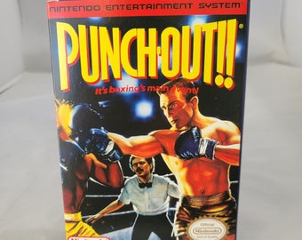 Könnte beinhalten: Eine Vintage-Spielkassette für das Nintendo Entertainment System für Punch-Out!! Das Cover zeigt einen Boxer in einem gelben und schwarzen Box-Outfit, der einen Schlag ausführt. Der Text "It's boxing's main event!" ist auf der Schachtel aufgedruckt.