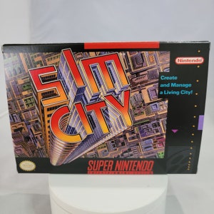 May include: A Super Nintendo Entertainment System game cartridge for SimCity. The box art features a colorful, 3D rendering of the game's title against a backdrop of a city skyline. The text "Create and Manage a Living City!" is printed on the right side of the box.