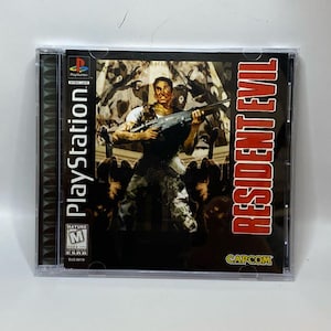 May include: A PlayStation game case for Resident Evil. The cover art shows a man with a rifle, set against a dark backdrop, with the game title in red. The case is in a clear plastic jewel case.