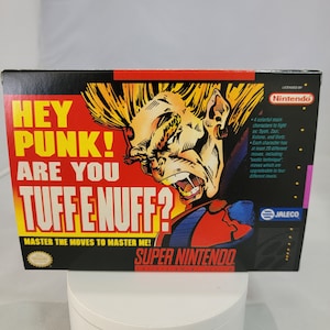 May include: A Super Nintendo game cartridge for the game Tuff E Nuff. The box art features a red and blue character with spiky hair and a menacing expression. The text on the box reads "Hey Punk! Are You Tuff E Nuff?" and "Master the moves to master me!"