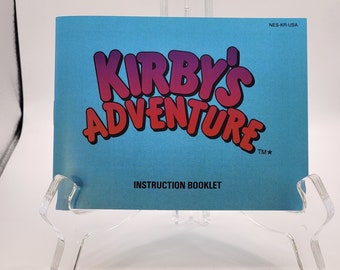 May include: A blue instruction booklet for the NES game "Kirby's Adventure" with the title in pink and red lettering. The booklet has the text "NES-KR-USA" and "INSTRUCTION BOOKLET" printed on it.