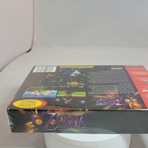Pu&ograve; includere: Copia sigillata di "The Legend of Zelda: Majora's Mask" per Nintendo 64. La scatola nera presenta grafica e testo colorati, incluso il logo Nintendo 64. Il gioco &egrave; ancora nella sua confezione di plastica originale.