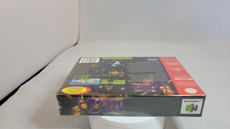 Pu&ograve; includere: Copia sigillata di "The Legend of Zelda: Majora's Mask" per Nintendo 64. La scatola nera presenta grafica e testo colorati, incluso il logo Nintendo 64. Il gioco &egrave; ancora nella sua confezione di plastica originale.