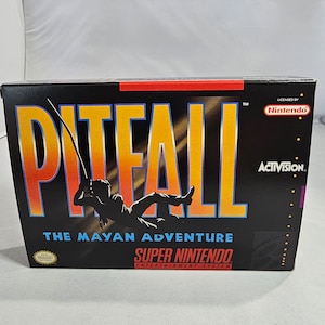May include: A black Super Nintendo game cartridge box with a red and yellow title: "Pitfall! The Mayan Adventure". The box features a silhouette of a person swinging on a rope with a jungle background. The game is licensed by Nintendo and published by Activision.