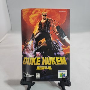 May include: A video game cartridge for the Nintendo 64 console featuring Duke Nukem 64. The cover art shows Duke Nukem, a muscular man with a red bandana, holding a gun and standing in front of an explosion. The text "DUKE NUKEM 64" is printed in yellow on a black background.