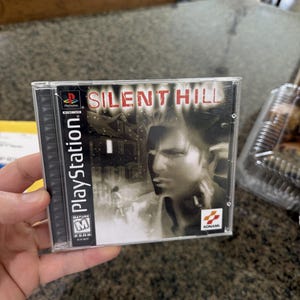 May include: A PlayStation game case for "Silent Hill." The cover art shows a man's face, a house, and the game's title in red. The case is clear plastic, and the game is rated M for Mature.